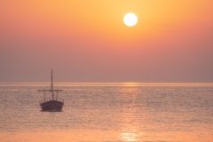 Boot im Sonnenaufgang vor dem Felsstrand der Cala Salpatx